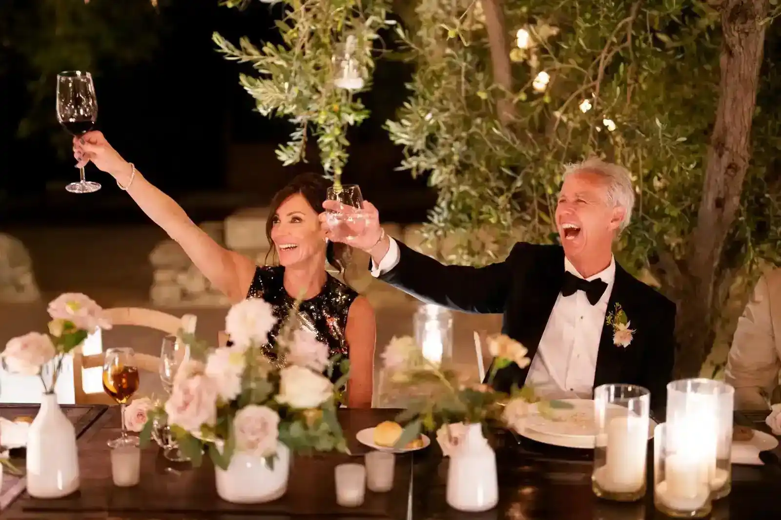 Guests raising a toast at an evening wedding dinner under olive trees in Puglia