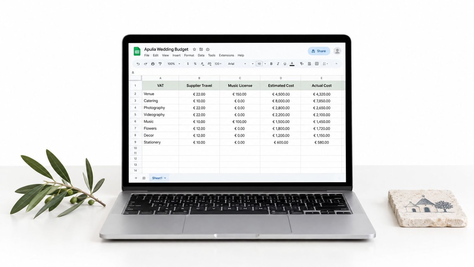 A silver laptop displaying an Apulia wedding budget spreadsheet on a white desk with an olive branch.